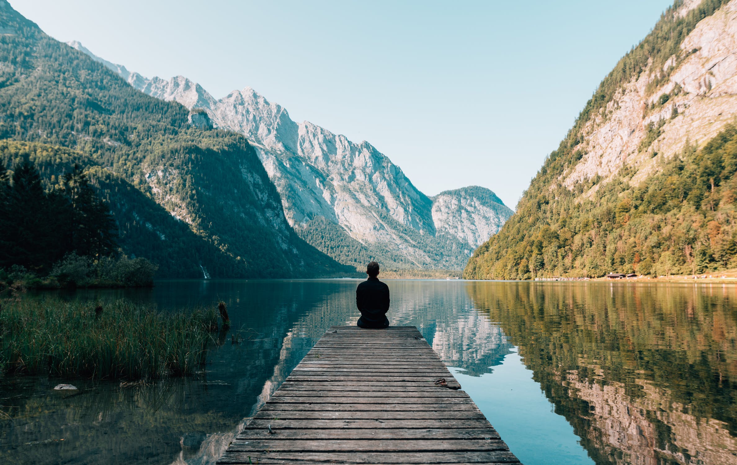 man sitting at the end of a doc on a lake reflecting on his life