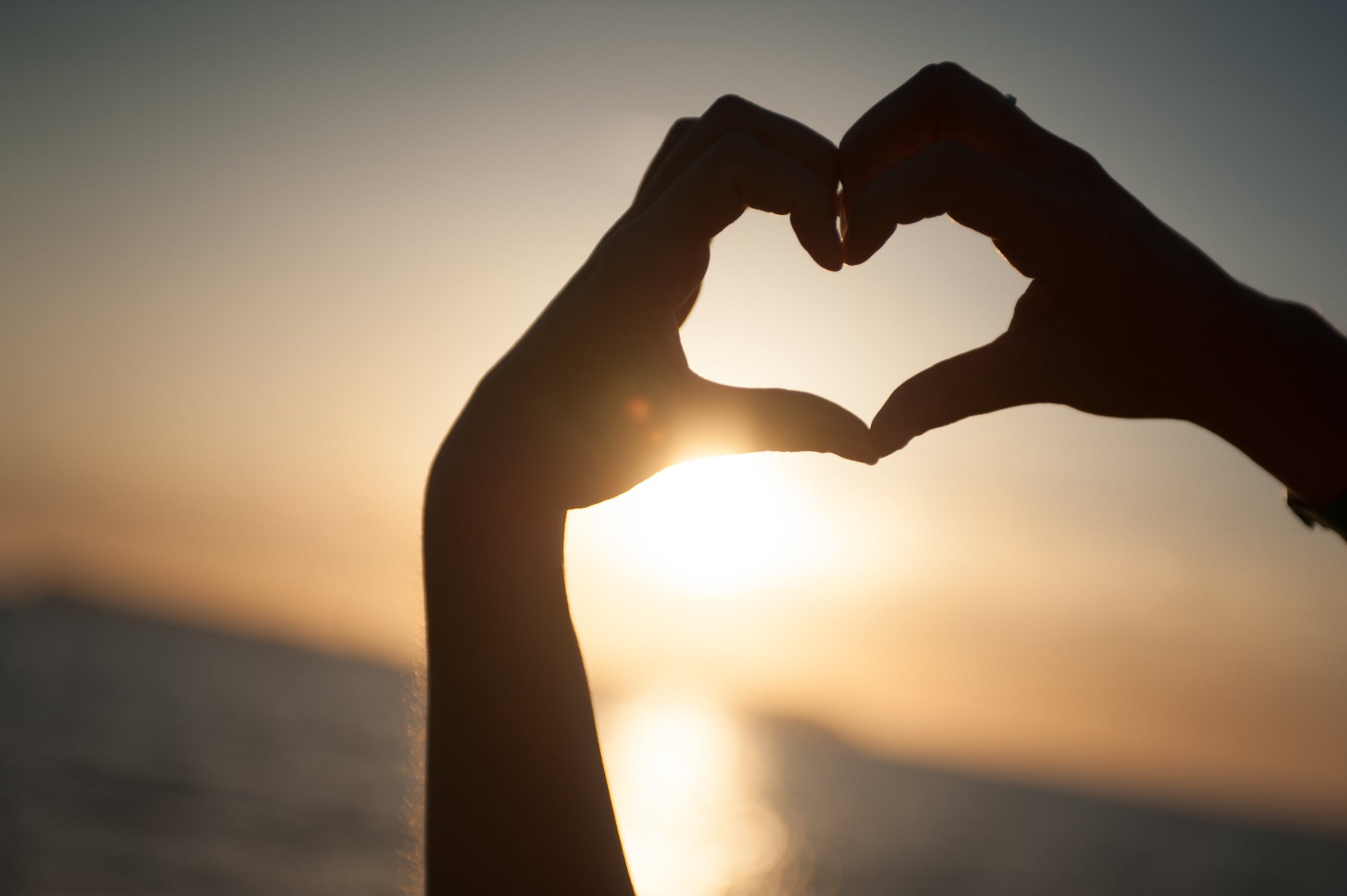 hands making a heart with sunset in the background